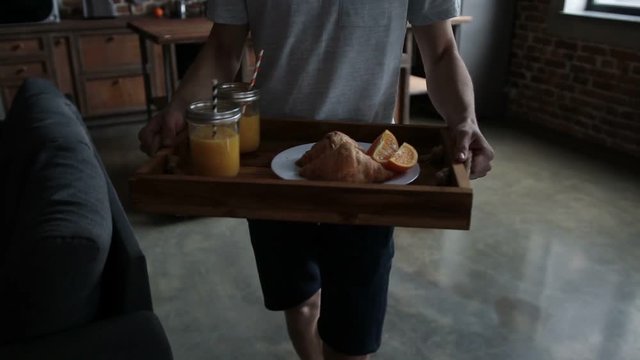 Man serving breakfast on wooden tray in bed