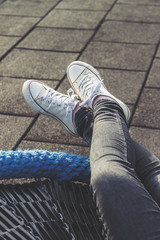 Woman relaxing outdoors, lying, legs crossed, wearing black jeans and white canvas sneakers