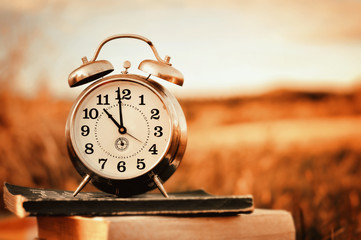 Old alarm clock over books, outside in autumn colors with copy space.