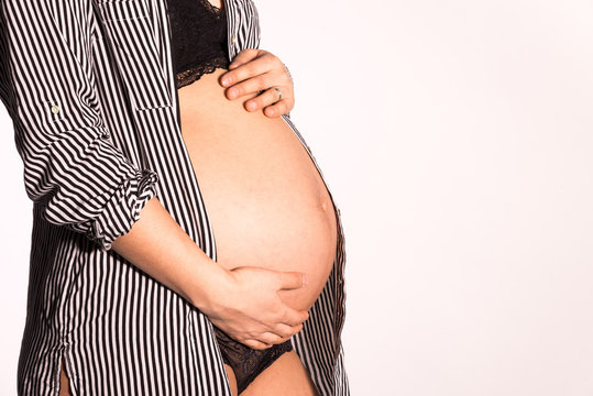 Pregnant woman with open shirt embracing belly and white background