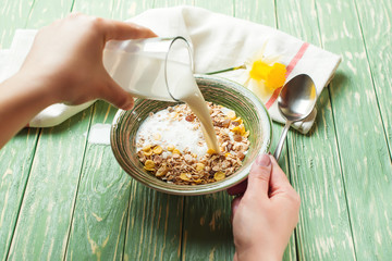 Healthy breakfast. Woman pouring milk into bowl with muesli.