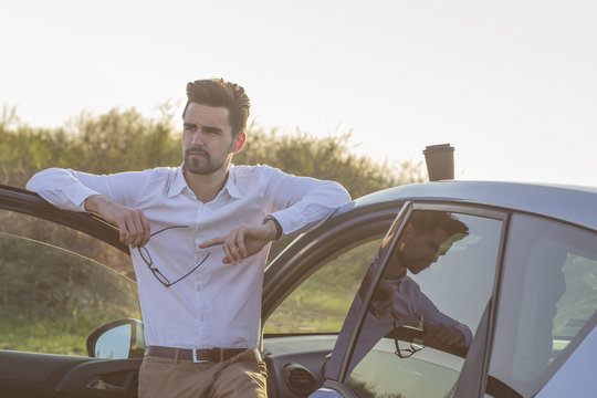 Young man with coffee to go on the roof of the car relaxing in nature