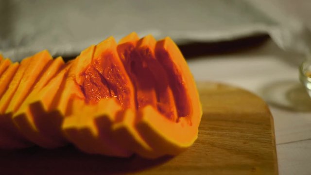Raw pumpkin pieces. Close up pumpkin slices on wooden board. Pumpkin slices with spices and herbs. Seasoning food on kitchen table. Vegetarian food. Cut pumpkin spice. Sliced vegetables