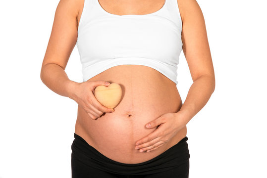 Pregnant woman holding heart in front of her bare belly