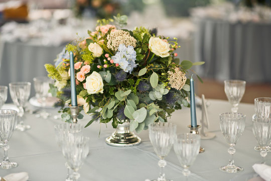 Little bouquet of roses and hydrangeas stands between blue candles on the table