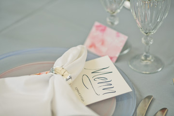 Card with lettering 'Menu' lies under white serviette on dinner plate