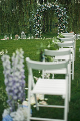 Look from behind at white chairs standing on the green lawn before wedding altar