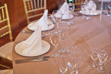 Crystal glasses stand before white plates on beige dinner table