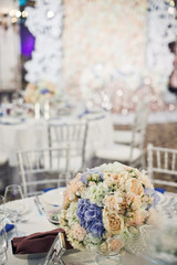 Bouquet of white roses and blue hydrangeas stands on the round dinner table