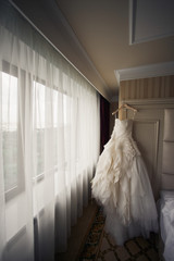 Fototapeta na wymiar Magnificent wedding dress hangs in beige hotel room