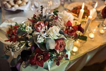 Bouquet of white and red flowers stands on the corner of dinner table