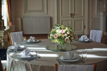 Little bouquet of roses and greenery stands in the middle of dinner table