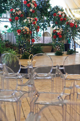 White chairs with transparent bacns stand before stage with flowers