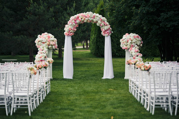 Arch with pink peonies stands before white chairs on the lawn