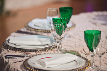Green glasses stand between plates on dinner table
