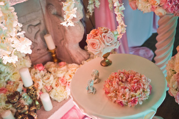 Little white table with pink flowers stands before fireplace