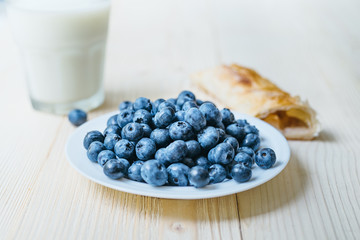 Rustic healthy breakfast with blueberry, small loaf and milk in a glass on a wooden table. Glass of milk with ripe berries. Healthy breakfast with vital vitamins.