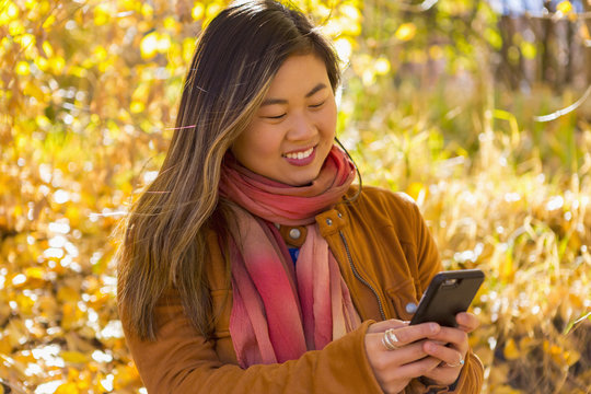 Asian woman texting on cell phone in autumn