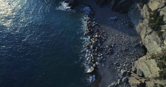 aerial overhead view of ocean mediterranean sea waves reaching and crashing on rocky shore beach, near Cinque terre National Park, Liguria, Italy. Sunny weather. 4k top view drone forward video shot