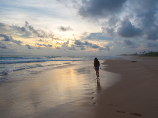 girl is walking along the beach at sunset