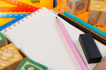 Blank notebook with school supplies on yellow plastic brick plate. Learning background concept.