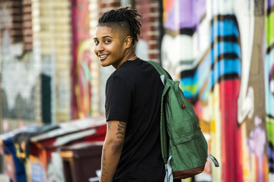 Smiling woman with tattoos and braids carrying backpack