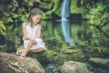 Little girl looks at the water sitting next to the bed of a river