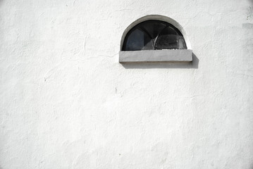 Old white masonry wall with half-moon, rustic window.