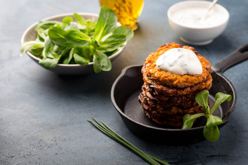 Sweet potato fritters in skillet served with fresh green salad, yogurt sauce and olive oil