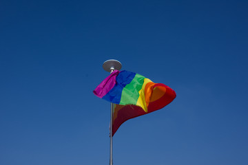 Rainbow flag waving on wind, blue sky background.