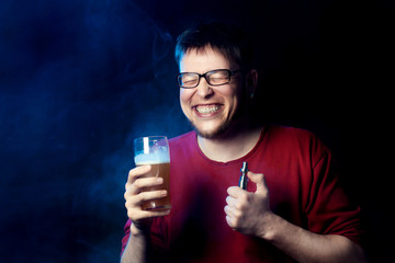 A laughing man in glasses with beer and an electronic cigarette in his hands. Dark background.
