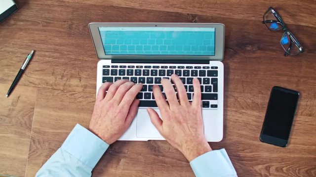 Man's hands typing on laptop keyboard on a wooden desck