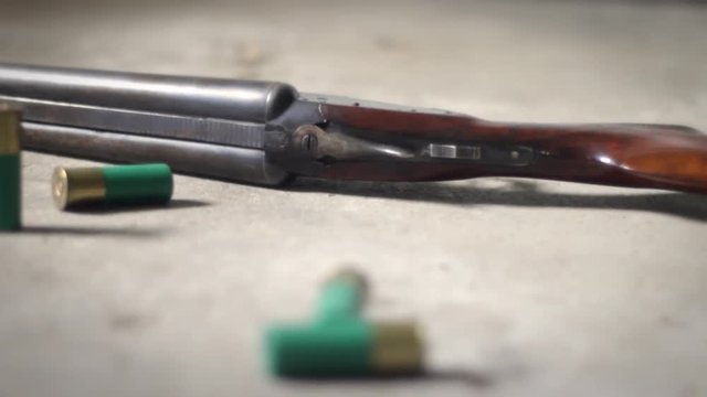 Camera pans by shotgun shells lying on concrete floor near double barrel shotgun - Angle 2