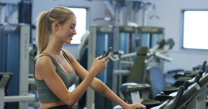 Young beautiful girl in a gym, shakes her legs on a cycling simulator, with a phone in her hand. The concept: to love sports, to attend a gym, proper nutrition, a slender body, to be healthy.