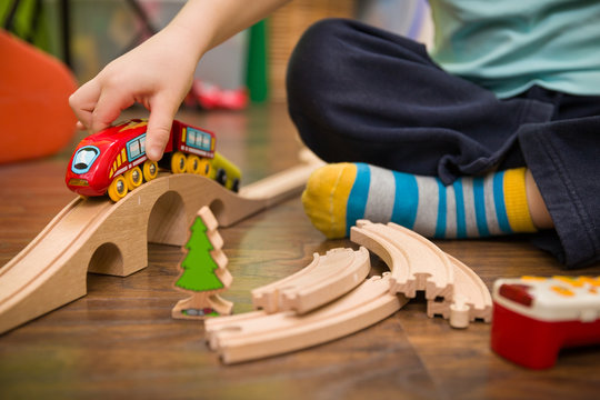 Close up on child's hands with toy train and railway in his room. Boy playing indoors.