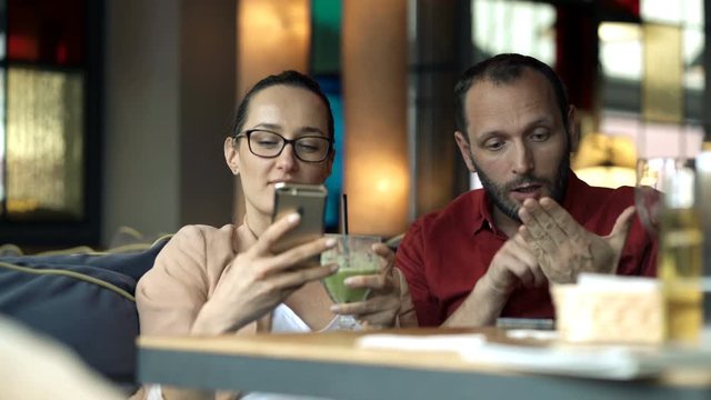 Man complaining about his girlfriend staring at smartphone in cafe

