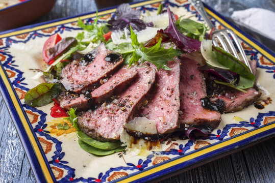 Traditional Italian Tagliata di Manzo Steak with Parmesan and Salad as close-up on a plate