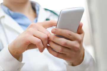 A female doctor texting on smartphone - obrazy, fototapety, plakaty