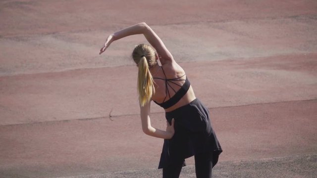 Girl doing warm-up at the stadium and performing lateral tilts, rear view, slow motion