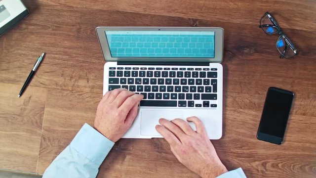 Man's hands typing on laptop keyboard on a wooden desck