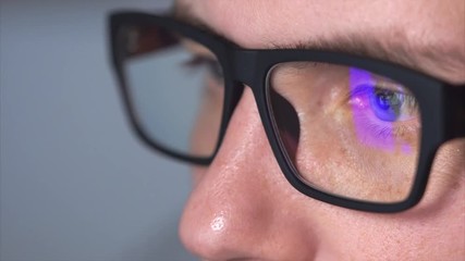 Close up shot of a man's eyes with eyeglasses looking at a monitor. The lenses of the glasses reflect the picture of the film that the young man is looking at his computer.