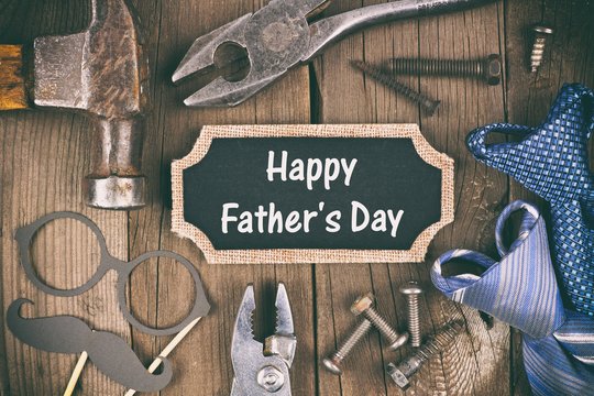 Happy Fathers Day message on a chalkboard tag with frame of tools and ties on a wooden background, vintage styling