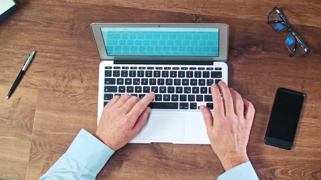 Man's hands typing on laptop keyboard on a wooden desck
