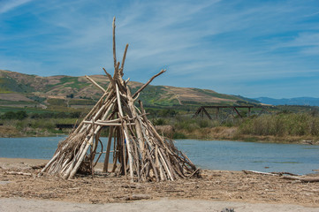 Fototapeta na wymiar Beach hut made of driftwood logs on estuary shoreline.