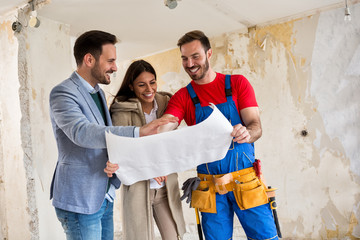 Beutiful young couple looking blueprints of their home with handyman
