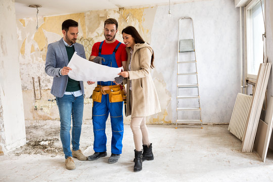 Beutiful young couple looking blueprints of their home with handyman