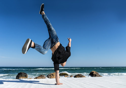 Young Athlete Doing One Arm Handstand On The Beach. Street Workout. Break Dancer Man In Action