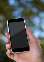 Hand with phone against blurry leaves