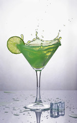 Splash in glass of green mint alcoholic cocktail drink with lime and ice cube