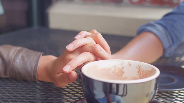 Close up of a couple holding hands across the table on a coffee date